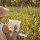 Une femme dessine à l'aquarelle dans une forêt