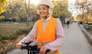 Une femme avec un casque et un gilet rétro-réfléchissant sur une trottinette électrique