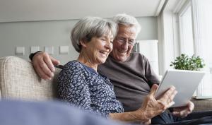 Une femme et un homme âgés sourient et utilisent une tablette