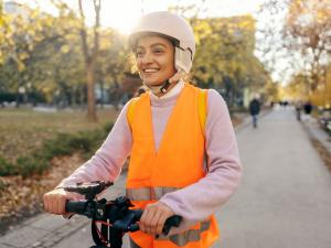Une femme avec un casque et un gilet rétro-réfléchissant sur une trottinette électrique