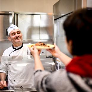 Un cuisinier sert un plat à la cantine