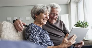 Une femme et un homme âgés sourient et utilisent une tablette