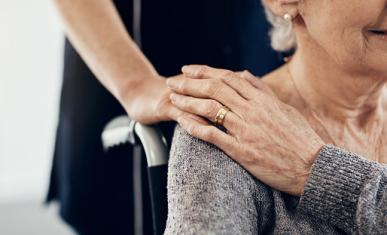 Main d'une jeune femme posée sur l'épaule d'une femme âgées en fauteuil