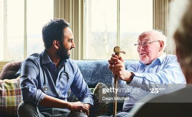 Sur un canapé, un homme jeune est en train de rire avec un homme âgé sous le regard d'une femme âgée