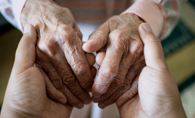 Gros plan sur les mains d'une personne âgée tenues par les mains d'une personne plus jeune